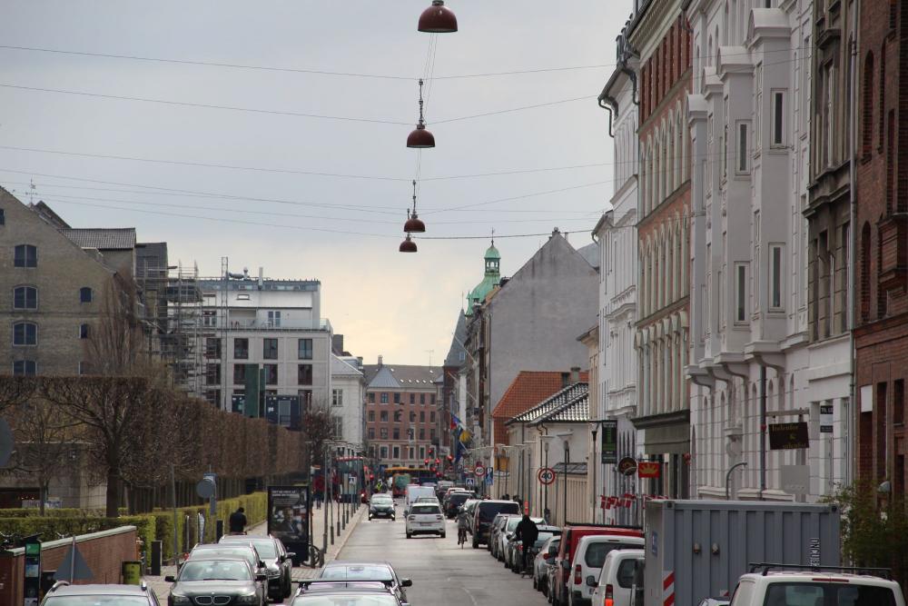 Et blik gennem Toldbodgade, hvor biler parkeret i begge sider af vejen og trafik i begge retninger efterlader meget lidt plads til cyklister
